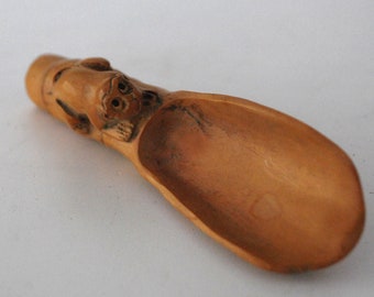May include: A wooden scoop with a carved monkey face on the handle. The scoop is light brown and has a smooth, polished finish. The scoop is designed for scooping tea leaves or other small items.
