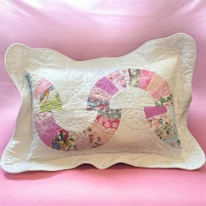 May include: A rectangular quilted pillow sham featuring a white base with a scalloped edge. The center displays a large, curved S-shaped applique pattern constructed from various floral and geometric fabric patches in shades of pink, blue, and green.