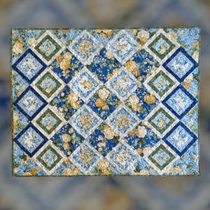 May include: A quilted blanket with a floral pattern in shades of blue, green, and yellow. The design features diamond shapes with floral and geometric patterns. The quilt is a rectangle.