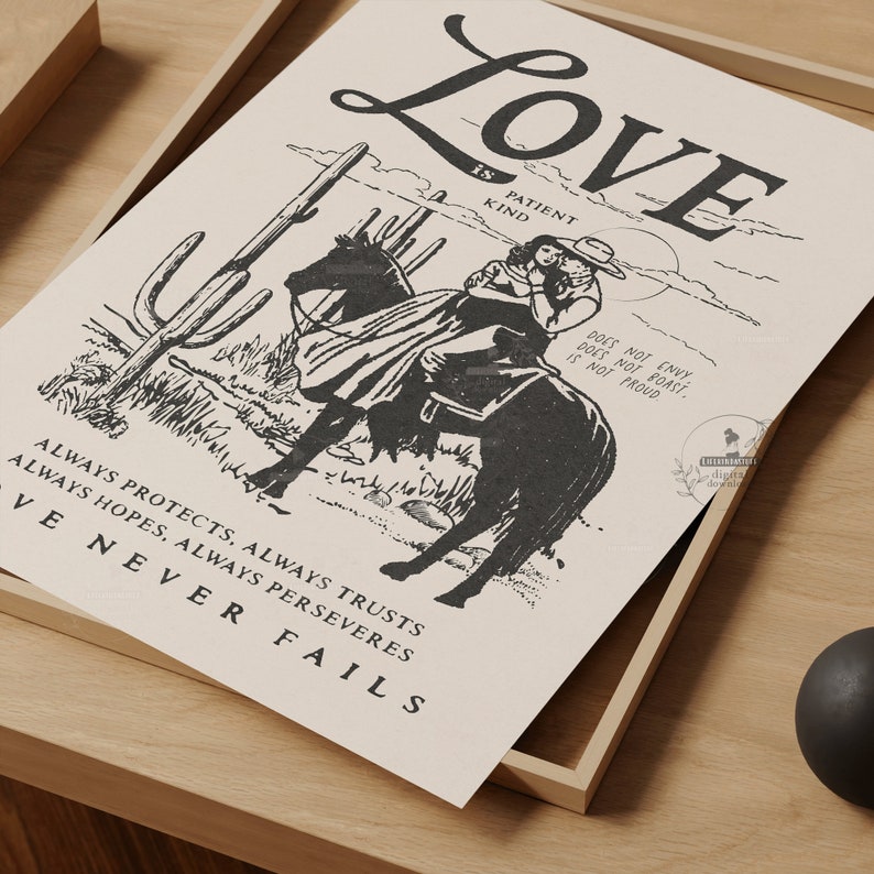 May include: A monochrome print depicting a cowboy and cowgirl on horseback in a desert scene. The print includes the word "Love" and other text describing love's qualities. The artwork is presented within a wooden frame, suitable for wall display.