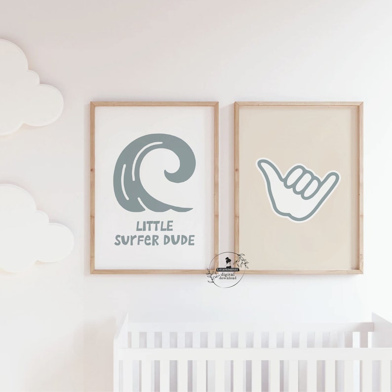 May include: Two framed prints with a surfing theme. One print features a stylized wave with the text "LITTLE SURFER DUDE" in a light blue color. The other print displays a light blue shaka hand gesture on a beige background.