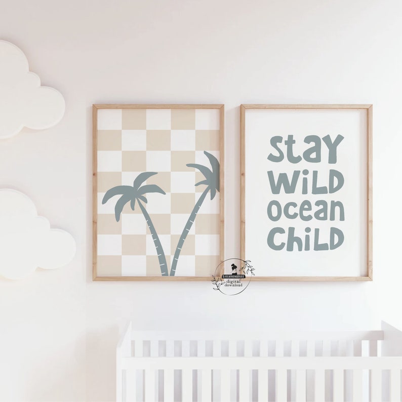 May include: Two framed wall art prints. One features a checkered pattern with palm tree silhouettes. The other print has the words "Stay Wild Ocean Child" in blue. Both are in wooden frames, suitable for a nursery or child's room.