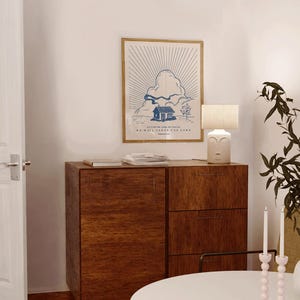 Peut inclure: Une affiche encadr&eacute;e avec une illustration bleue et blanche d'une maison, de nuages et de rayons de soleil. Le texte dit &laquo; AS FOR ME AND MY HOUSE WE WILL SERVE THE LORD &raquo;. Un meuble en bois et une lampe avec un visage sont &eacute;galement visibles.
