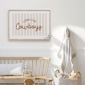 May include: A beige and brown striped poster with the text "Long Live Cowboys" in brown lettering. The poster is hanging on a white wall in a nursery.
