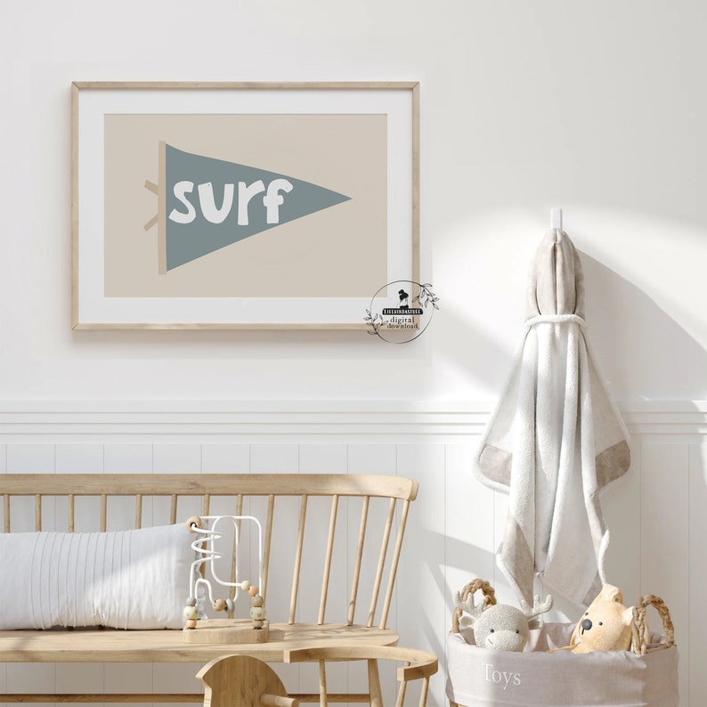 May include: A framed wall art print featuring a blue pennant with the word "surf" in white. The pennant is set against a beige background. The artwork is in a light wooden frame, suitable for a coastal or beach-themed nursery or bedroom.