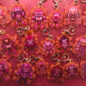May include: A collection of 15 pink and red robot character keychains with heart-shaped details. The keychains are made of clear plastic and feature different robot characters with varying poses.