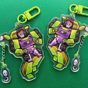 May include: A white ceramic mug with a black handle and the text "But First, Coffee" in a bold, black font. The mug is set against a blurred background, suggesting a cozy setting.