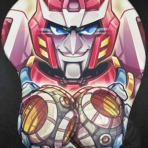 May include: Ergonomic mouse pad featuring a stylized illustration of a robot character with a red and white helmet, blue eyes, and a smiling expression. The design includes detailed mechanical elements in shades of yellow, orange, and green.