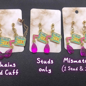 Puede incluir: Pendientes con tachuelas, cadenas y puños dorados. Los pendientes presentan un diseño rectangular con un patrón turquesa y dorado, conectados por formas geométricas rosas. Los pendientes tienen gemas rosas en forma de lágrima. El texto de la imagen dice "Chains and Cuff", "Studs only" y "Mismatched (1 Stud & 1 Cuff)".