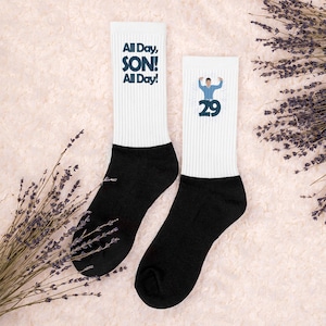 May include: Two white socks with black heels and toes. One sock has the text "All Day, SON! All Day!" in navy blue. The other sock has a graphic of a person and the number 29 in navy blue.