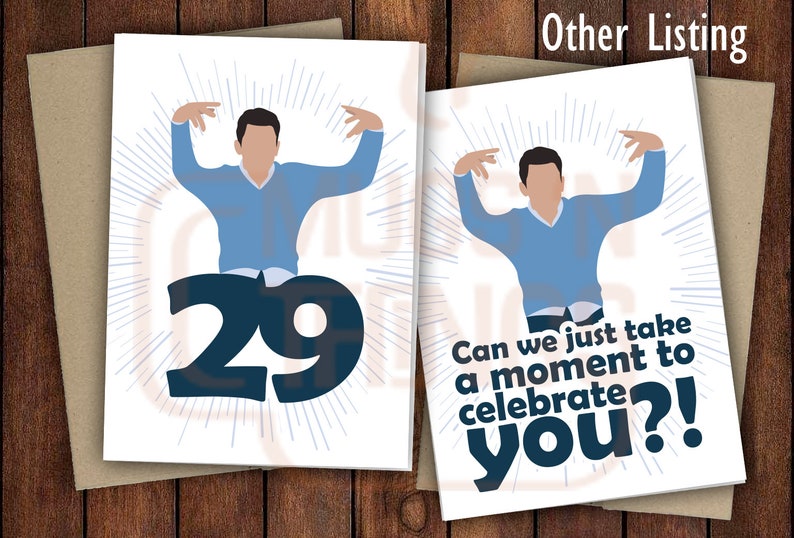 May include: A white greeting card with a blue illustration of a person with arms raised in the air. The number 29 is in the background. The text on the card reads "Can we just take a moment to celebrate you?!"