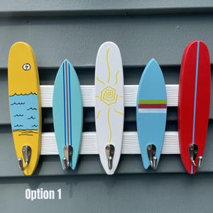May include: A wall-mounted hook rack featuring five surfboard-shaped wooden plaques in yellow, light blue, white, medium blue, and red, each with a silver metal hook. The text "Option 1" is printed in white at the bottom of the image.