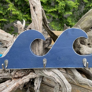 May include: A navy blue wooden wave-shaped coat rack with three silver hooks. The rack is mounted on a weathered tree branch.