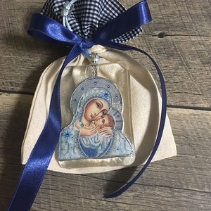 May include: A religious icon pendant featuring the Virgin Mary and baby Jesus, presented in a beige fabric pouch with a navy blue gingham drawstring and a navy blue satin ribbon. The icon has blue and silver accents.