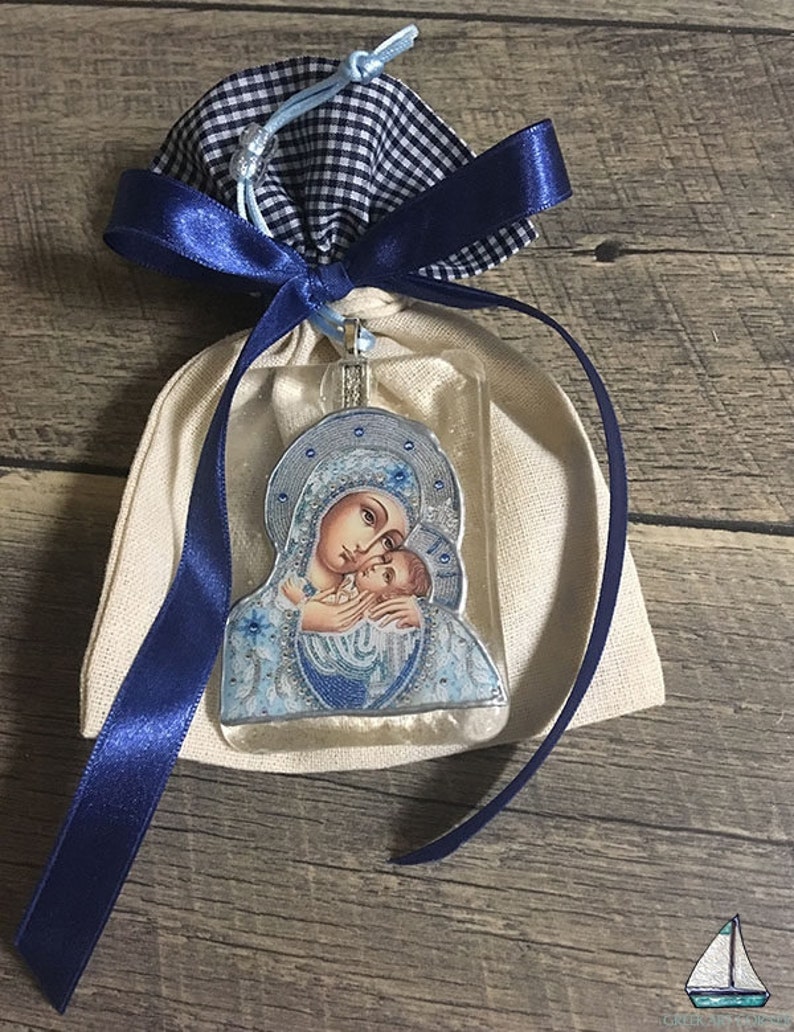 May include: A religious icon pendant featuring the Virgin Mary and baby Jesus, presented in a beige fabric pouch with a navy blue gingham drawstring and a navy blue satin ribbon. The icon has blue and silver accents.
