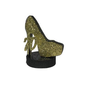 Pu&ograve; includere: Una statuetta decorativa a forma di scarpa con tacco alto. La scarpa &egrave; ricoperta di glitter dorati e ha un bordo nero. Poggia su una base nera strutturata e presenta un dettaglio a fiocco. Il design &egrave; glamour e accattivante.