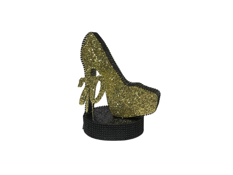Pu&ograve; includere: Una statuetta decorativa a forma di scarpa con tacco alto. La scarpa &egrave; ricoperta di glitter dorati e ha un bordo nero. Poggia su una base nera strutturata e presenta un dettaglio a fiocco. Il design &egrave; glamour e accattivante.