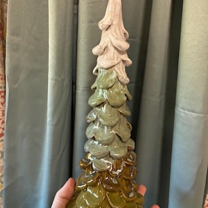 May include: A tall, conical ceramic sculpture shaped like a tree with overlapping, petal-like layers. The color transitions from a deep olive green at the wide base to a lighter sage green in the middle, ending in a pale, creamy white at the top.