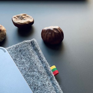 May include: A gray felt laptop sleeve with a small yellow, green, and red flag attached. Four brown chestnuts are scattered on a gray surface.