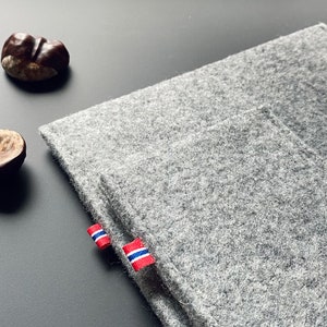 May include: A gray felt laptop sleeve with a red, white, and blue fabric tag. The sleeve is folded in half and has a pocket on the front.