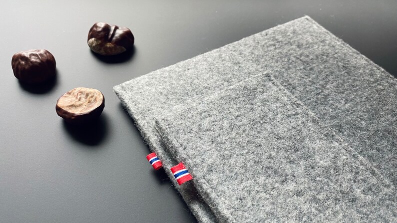 May include: A gray felt laptop sleeve with a red, white, and blue fabric tag. The sleeve is folded in half and has a pocket on the front.