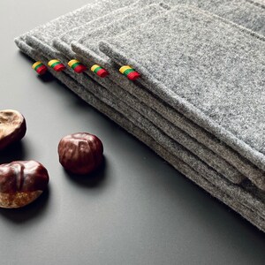 May include: A stack of gray felt coasters with yellow, green, and red ribbon accents. The coasters are arranged on a gray surface with three brown chestnuts.