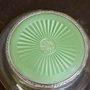 K&ouml;nnte beinhalten: Eine antike Glas-Schmuckschatulle mit silberfarbenem Rand und einem gr&uuml;nen Deckel mit Sonnenstrahlen-Design.