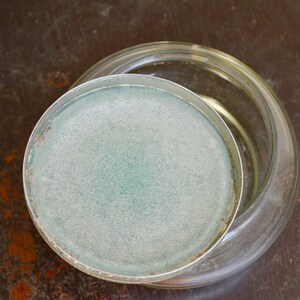 K&ouml;nnte beinhalten: Ein klares Glasgef&auml;&szlig; mit einem mattierten Deckel. Der Deckel hat einen hellblauen Farbton.