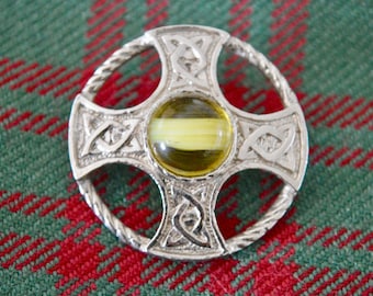 Puede incluir: Un broche de cruz celta de plata con un centro de vidrio amarillo y verde.