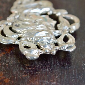 May include: A silver-toned metal ornament with a floral design. The ornament has a detailed, intricate design with a raised centre.
