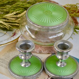 K&ouml;nnte beinhalten: Zwei silberne Kerzenhalter mit gr&uuml;nen Sockeln und ein Glasgef&auml;&szlig; mit gr&uuml;nem Deckel. Das Gef&auml;&szlig; und die Kerzenhalter haben einen silbernen Rand.