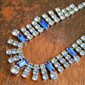 Puede incluir: Un collar de plata con diamantes de imitación azules y transparentes. El collar tiene un diseño graduado con un colgante central.