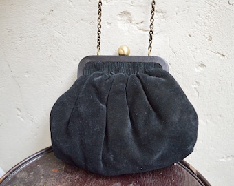 Może przedstawiać: Czarna aksamitna torebka typu clutch z złotym łańcuszkiem i drewnianą ramą.