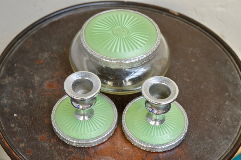 K&ouml;nnte beinhalten: Ein Set aus drei Vintage-Schminkutensilien in Gr&uuml;n und Silber. Das Set enth&auml;lt ein rundes Glasgef&auml;&szlig; mit einem gr&uuml;nen Deckel und zwei passende Kerzenhalter mit gr&uuml;nen Sockeln.