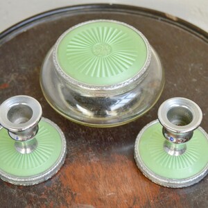 K&ouml;nnte beinhalten: Ein Vintage-Schminktisch-Set mit einem Glasgef&auml;&szlig; mit gr&uuml;nem Deckel und zwei passenden Kerzenhaltern mit gr&uuml;nen Sockeln.