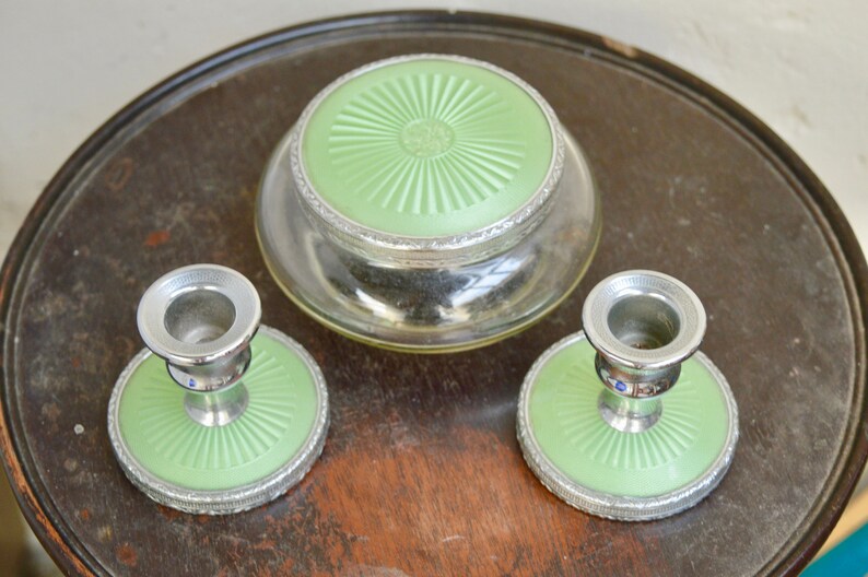 K&ouml;nnte beinhalten: Ein Vintage-Schminktisch-Set mit einem Glasgef&auml;&szlig; mit gr&uuml;nem Deckel und zwei passenden Kerzenhaltern mit gr&uuml;nen Sockeln.