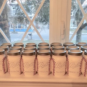 May include: A row of white mason jars with red stitching, painted to look like baseballs. Each jar has the word "Ball" and "Mason" printed on the front.