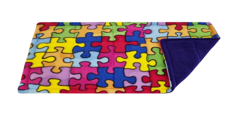 May include: A colourful puzzle piece patterned weighted blanket with a soft purple fleece lining. The blanket is designed to provide sensory input and comfort.