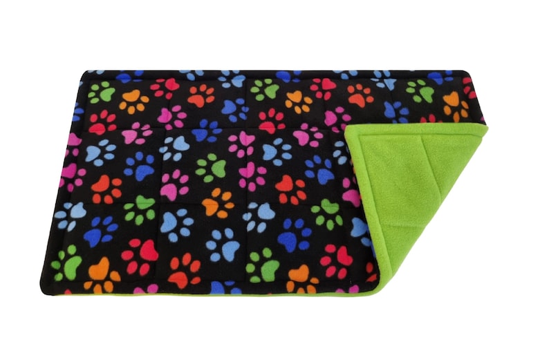 May include: A black pet bed with a colourful paw print pattern on one side and a solid green fleece on the other side.