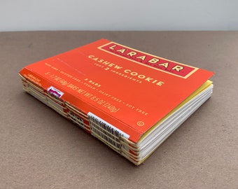 May include: A box of Larabar Cashew Cookie bars. The box is orange with yellow text and a white label. The box contains 5 bars, each weighing 8.5 ounces (240 grams). The bars are gluten-free, vegan, dairy-free, and soy-free.