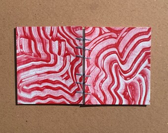 May include: A small, red and white patterned notebook with a spiral binding. The notebook has a marbled design.