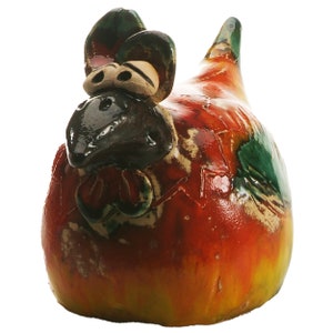 May include: A ceramic chicken figurine featuring a glossy, multi-coloured glaze in shades of vibrant red, yellow, and green. The sculpture has a dark brown beak, prominent eyes, and a textured surface with visible cracks in the glaze finish.