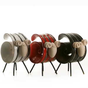 May include: Three ceramic sheep figurines with striped bodies and black metal legs. The sheep are in white, red, and black.
