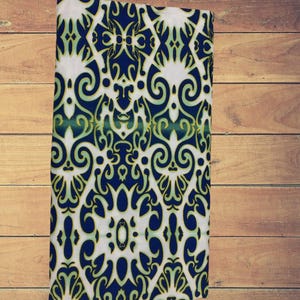 May include: A white fabric with a blue and green patterned design. The pattern is a repeating geometric design with swirls and curves.