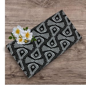May include: A folded black and white patterned fabric with a geometric design. The fabric is decorated with white flowers with yellow centers and green leaves. The fabric is resting on a wooden surface.