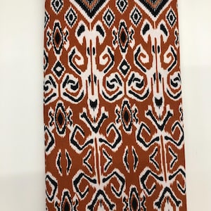 May include: Brown fabric with a white and black geometric pattern. The pattern features a repeating design of diamonds, zigzags, and swirls.