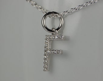 Può includere: Una collana color argento con un ciondolo a forma di lettera "F". Il ciondolo è incastonato con piccole pietre preziose trasparenti. La catena è anch'essa argentata e presenta un delicato design a maglie.
