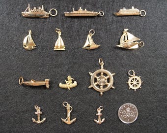May include: A collection of gold-toned metal charms featuring nautical themes, including various ships, sailboats, a canoe, a ship's wheel, and anchors. A circular coin with the number 5 is included for scale, measuring approximately 0.9 inches in diameter.