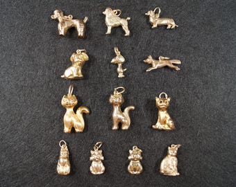 May include: A collection of thirteen gold-toned metal charms shaped like various animals, including dogs and cats. Each charm features a small loop at the top for attachment, with detailed textures representing the fur and features of each animal.