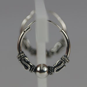 May include: A pair of silver hoop earrings. Each earring features decorative detailing on either side of a central silver bead. The design includes curved, stylized elements and textured accents, creating a detailed and ornate appearance.